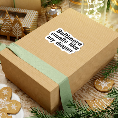 Funny kiss-cut sticker on a wrapped gift box, reading 'Baltimore Smells Like My Diaper' for a playful holiday vibe.