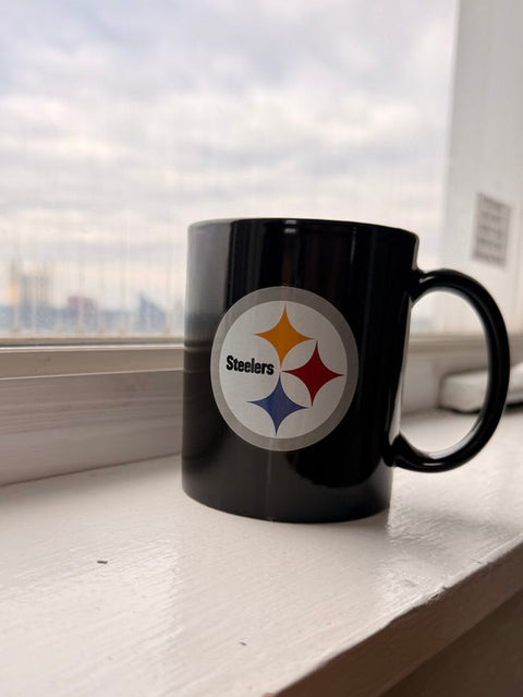 Black mug with a Pittsburgh Steelers sports team logo on a windowsill