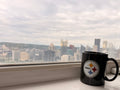 Black mug with a logo on a windowsill with a Pittsburgh cityscape view